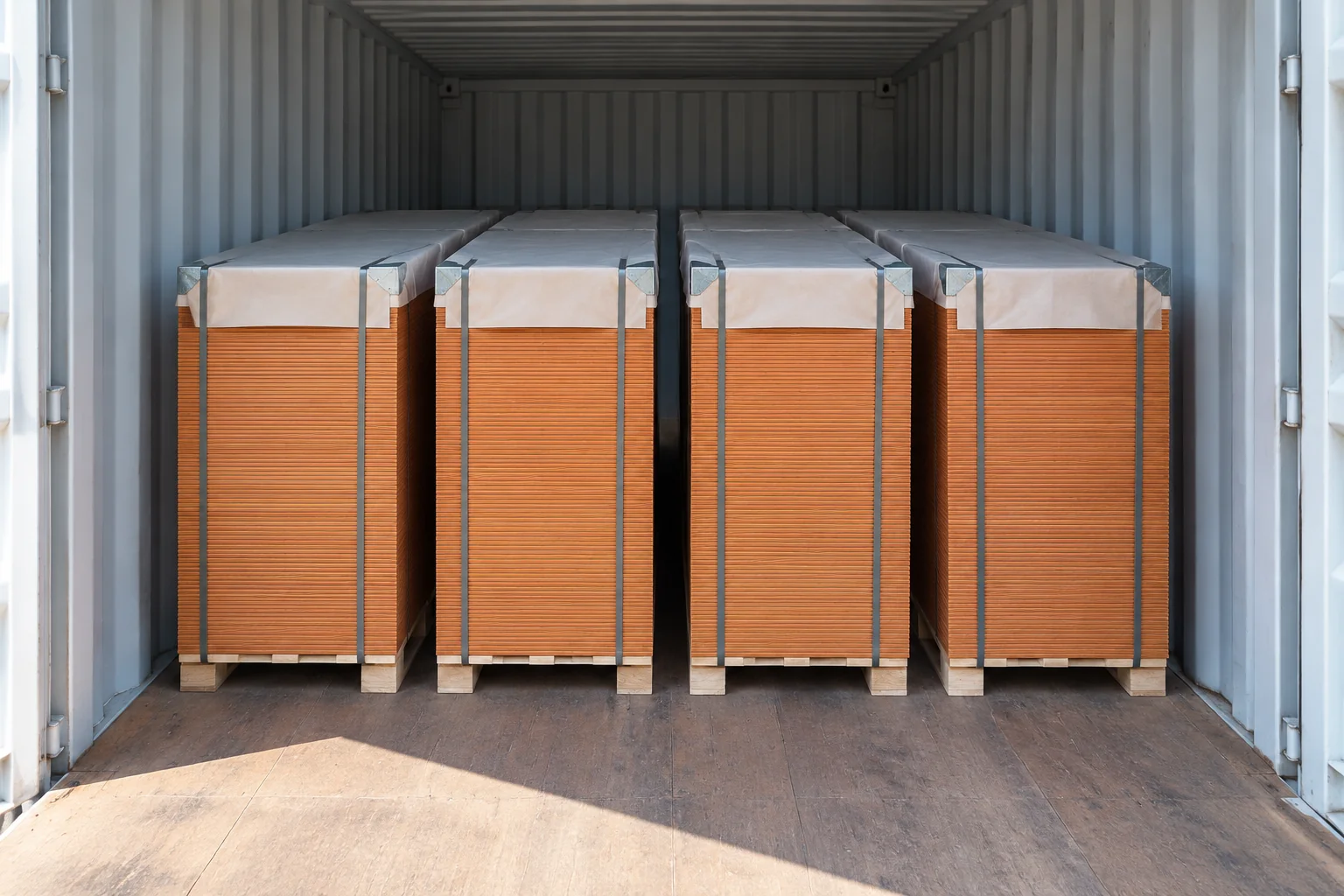 Four strapped packs of film-faced plywood on pallets with protective top sheets inside a shipping container