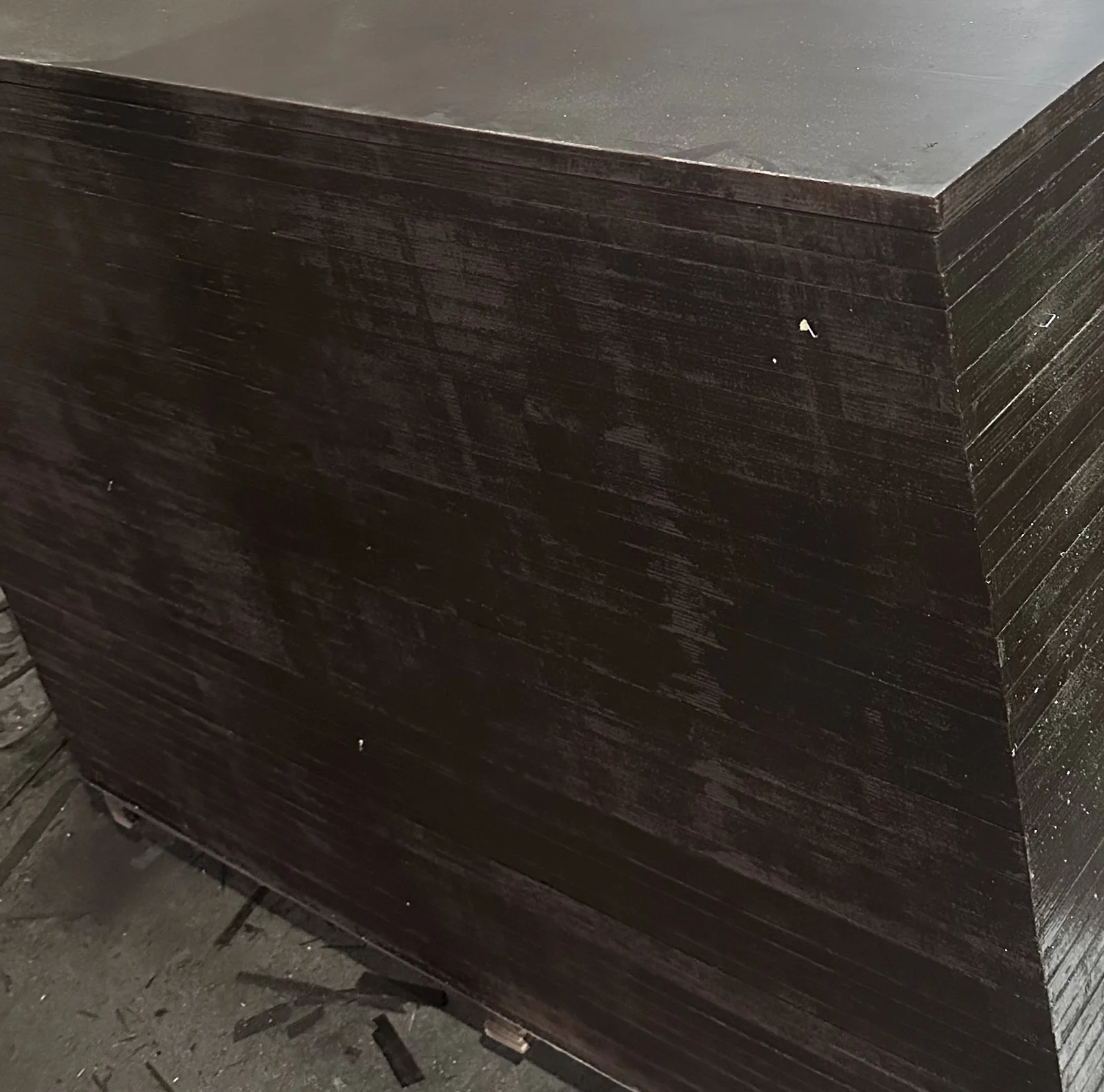 Corner of a tall pack of film-faced plywood with a glossy top face and dark sealed edges