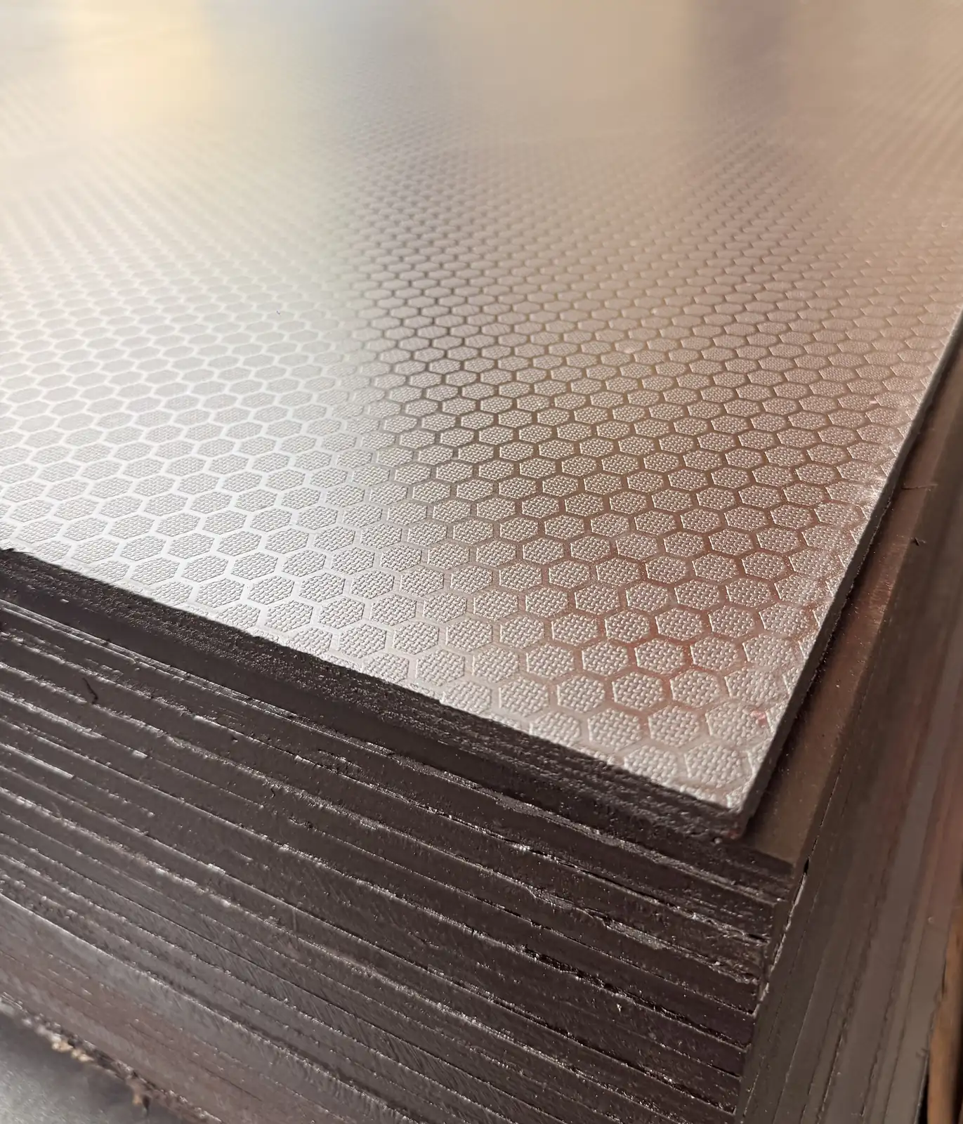 Corner of a stack of hexagon-pattern anti-slip plywood showing the embossed face and dark sealed edges